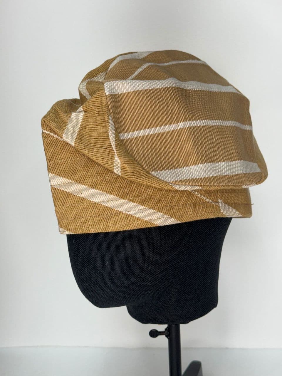 Mustard yellow and white striped Aso Oke fila hat on a black mannequin head.