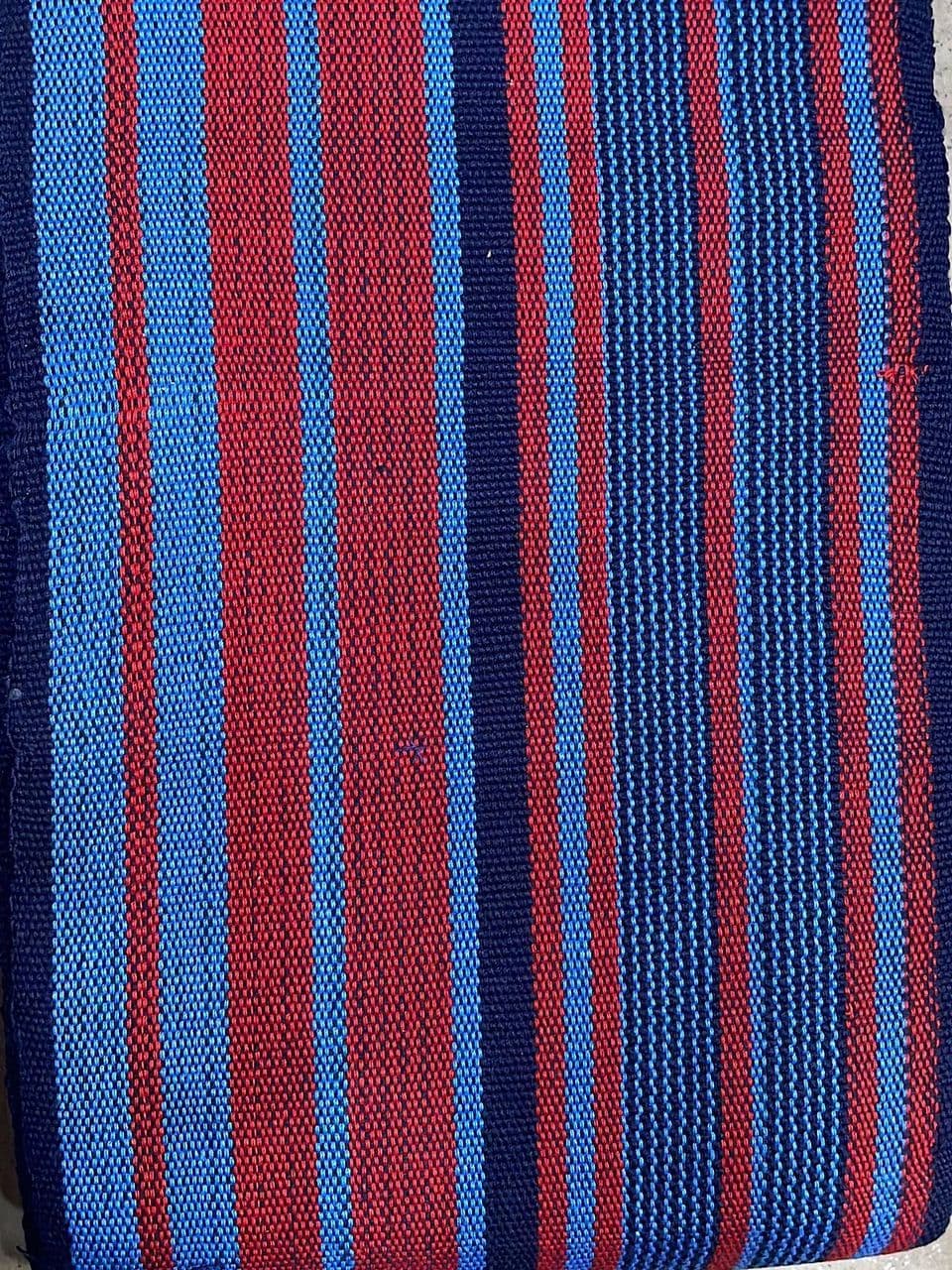 Close-up of a woven fabric featuring vertical stripes in red, light blue, and navy blue.