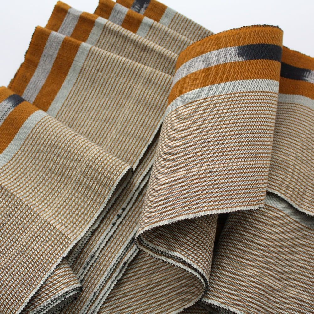 Folded ochre and white striped fabric featuring fine horizontal lines and dark grey accents.