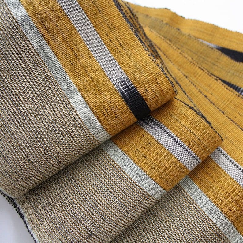 Textured woven fabric with mustard yellow, light gray, and black stripes folded in layers.