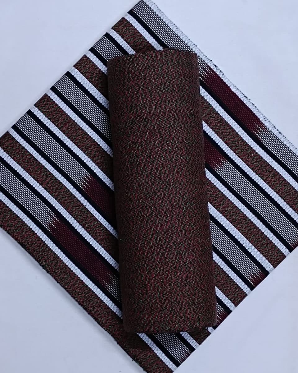 Rolled maroon textured fabric atop a flat maroon, black, and white striped textile.