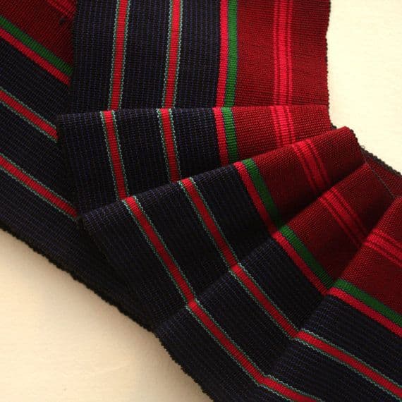 Navy blue, red, and green striped woven fabric ribbon fanned out on a light background.