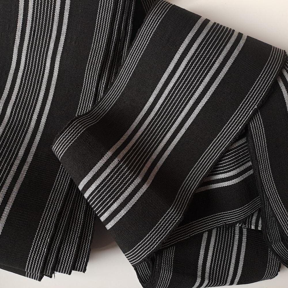 Folded black kaku-obi belt featuring a traditional pattern of thin, vertical white and silver stripes.